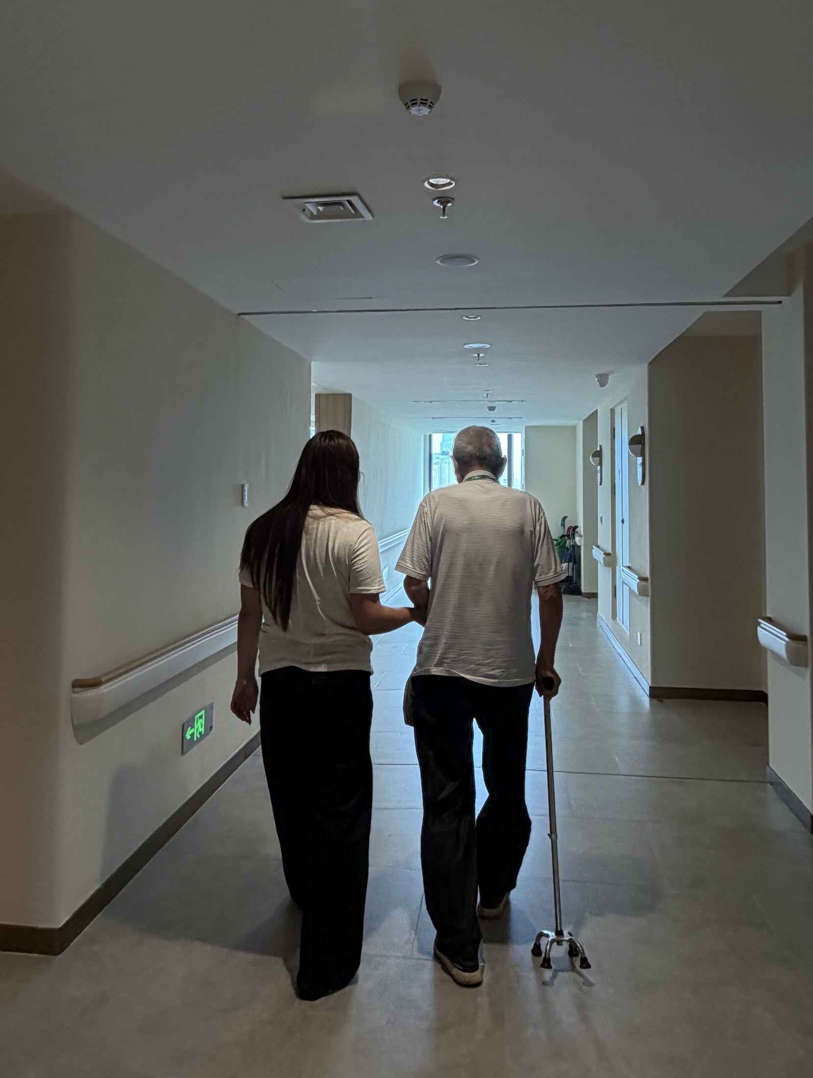 Jessica accompanying an older adult with a cane along an indoor hallway