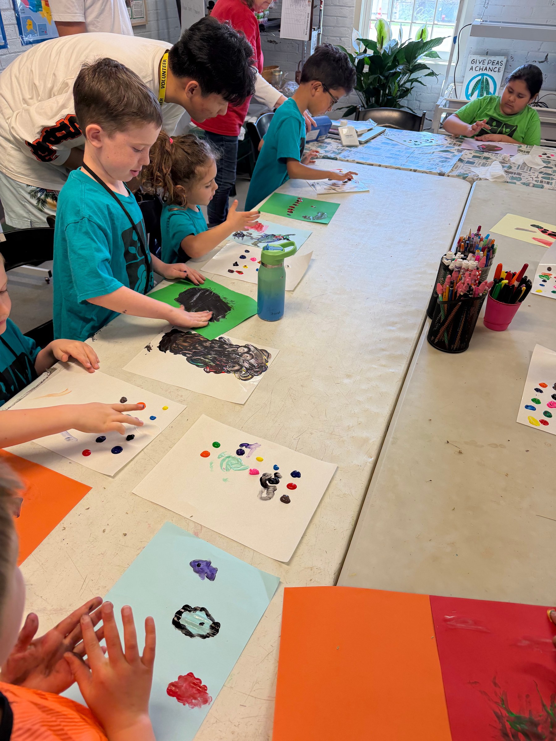 Children creating animal habitat paintings around a classroom table